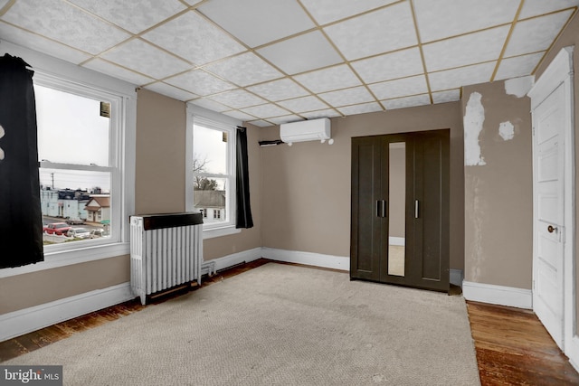 empty room with hardwood / wood-style flooring, a paneled ceiling, radiator heating unit, and a wall unit AC