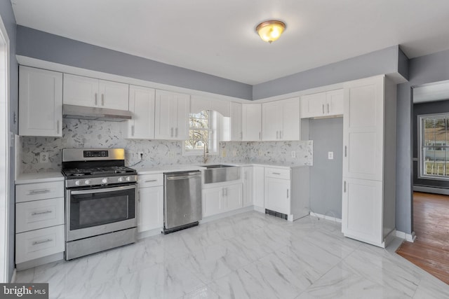 kitchen with light countertops, marble finish floor, under cabinet range hood, and stainless steel appliances