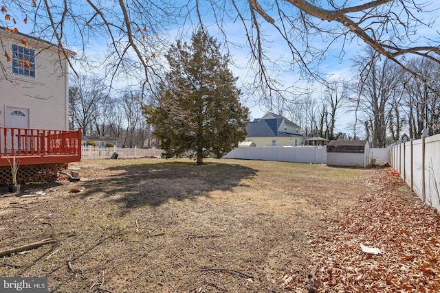 view of yard with a storage unit, a deck, an outbuilding, and a fenced backyard