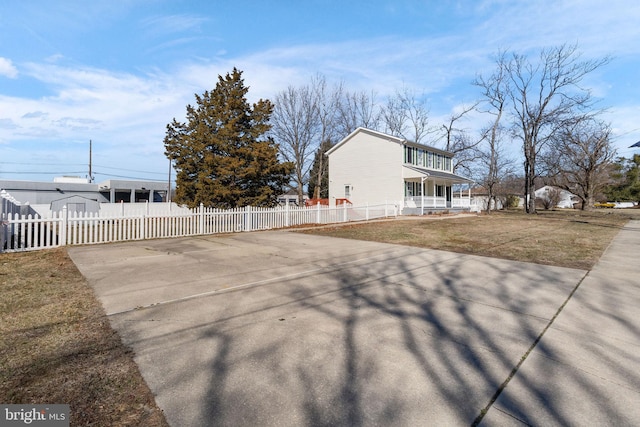 view of property exterior with a fenced front yard, covered porch, driveway, and a yard