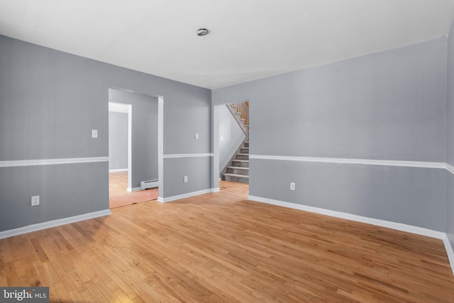 unfurnished room featuring a baseboard heating unit, baseboards, light wood-style floors, and stairs