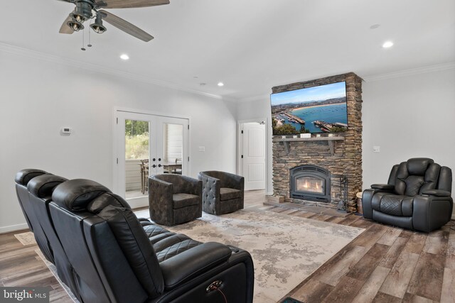 living room featuring wood-type flooring, a stone fireplace, crown molding, ceiling fan, and french doors