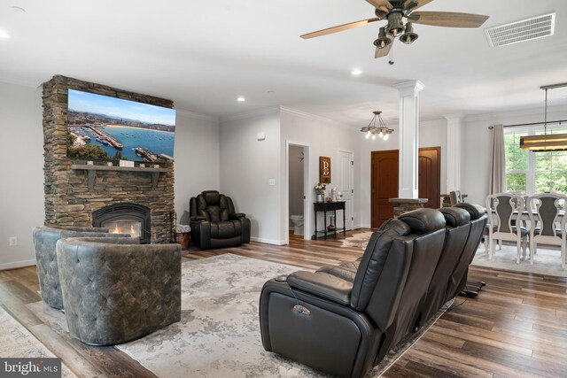 living room featuring ceiling fan with notable chandelier, a fireplace, wood-type flooring, decorative columns, and ornamental molding