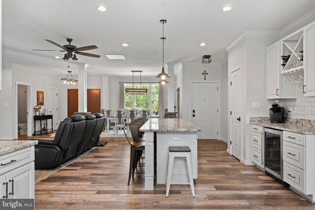 kitchen featuring light stone counters, wine cooler, hanging light fixtures, white cabinetry, and a center island