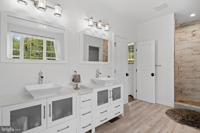 bathroom with a healthy amount of sunlight, wood-type flooring, a shower with door, and vanity