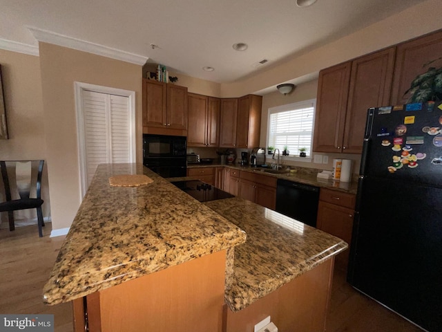 kitchen featuring a center island, black appliances, sink, and light stone countertops