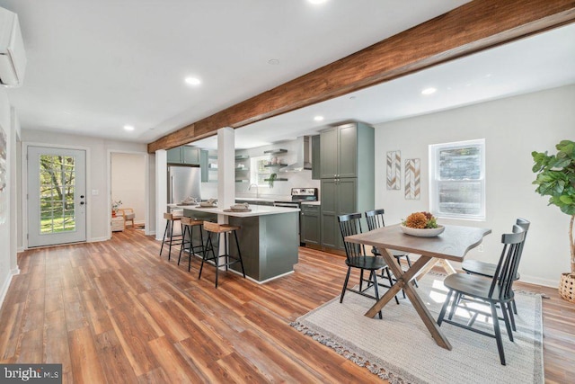 kitchen with a breakfast bar, beamed ceiling, a center island, light hardwood / wood-style flooring, and wall chimney exhaust hood