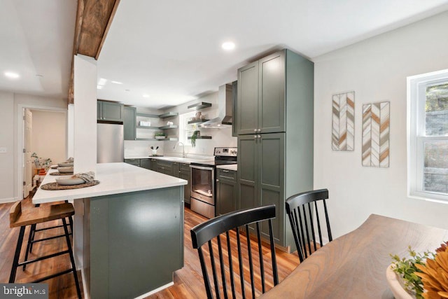 kitchen with a center island, light hardwood / wood-style flooring, stainless steel appliances, a kitchen breakfast bar, and wall chimney exhaust hood