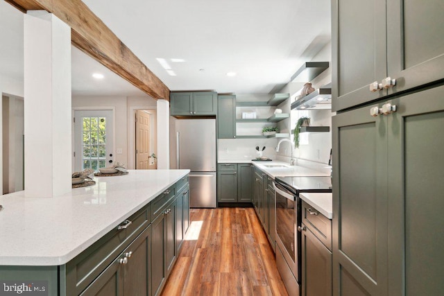 kitchen with appliances with stainless steel finishes, light stone counters, light wood-type flooring, sink, and wall chimney range hood