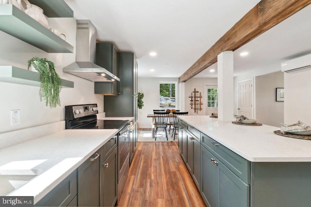 kitchen with a wall unit AC, beam ceiling, wall chimney exhaust hood, dark hardwood / wood-style flooring, and stainless steel range with electric stovetop