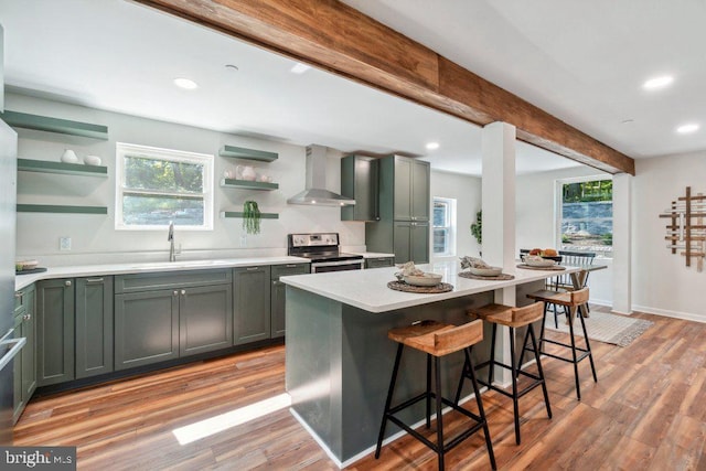 kitchen with wall chimney exhaust hood, stainless steel range with electric stovetop, light hardwood / wood-style flooring, and a kitchen island