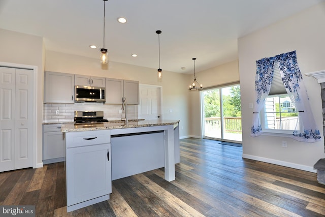 kitchen with a kitchen island with sink, dark wood-type flooring, stainless steel appliances, and pendant lighting