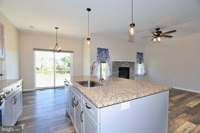 kitchen featuring decorative light fixtures, a fireplace, a kitchen island with sink, dark wood-type flooring, and sink