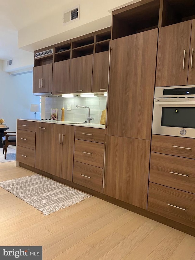 kitchen with oven, open shelves, visible vents, and light wood finished floors