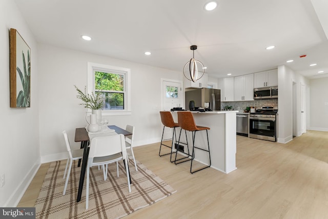 kitchen featuring pendant lighting, white cabinetry, stainless steel appliances, a center island, and light hardwood / wood-style floors