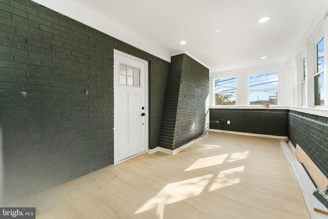 interior space featuring ornamental molding, light hardwood / wood-style floors, and brick wall