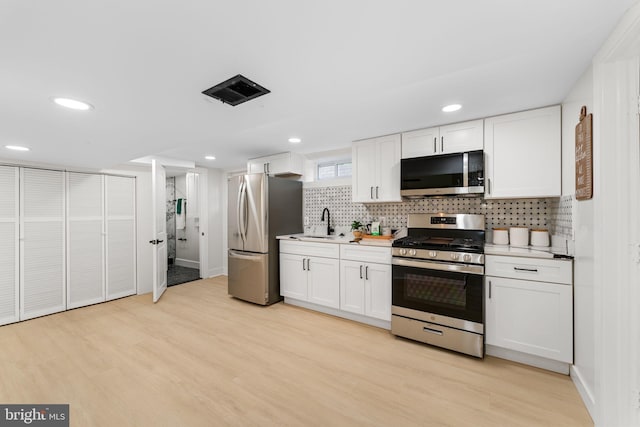 kitchen featuring appliances with stainless steel finishes, white cabinetry, decorative backsplash, and light hardwood / wood-style floors