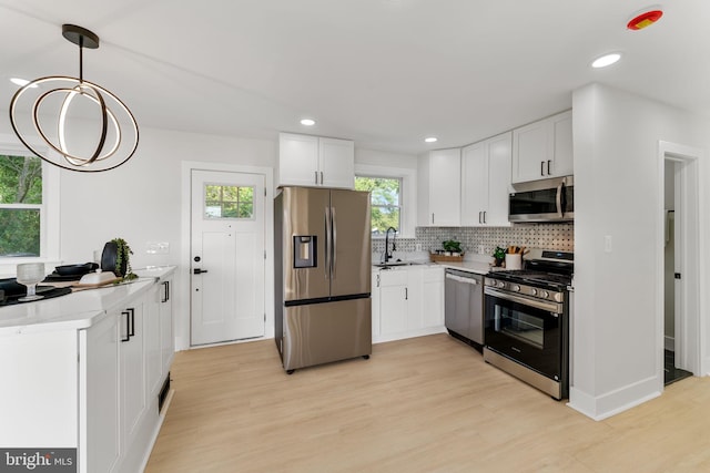 kitchen with light wood-type flooring, white cabinetry, decorative light fixtures, sink, and appliances with stainless steel finishes