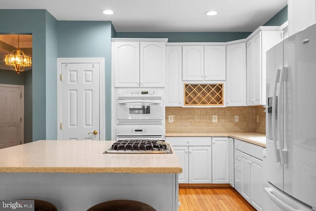 kitchen with white cabinetry, light hardwood / wood-style floors, hanging light fixtures, and white appliances