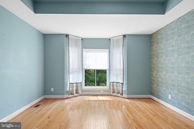 empty room featuring an accent wall, hardwood / wood-style flooring, visible vents, and baseboards