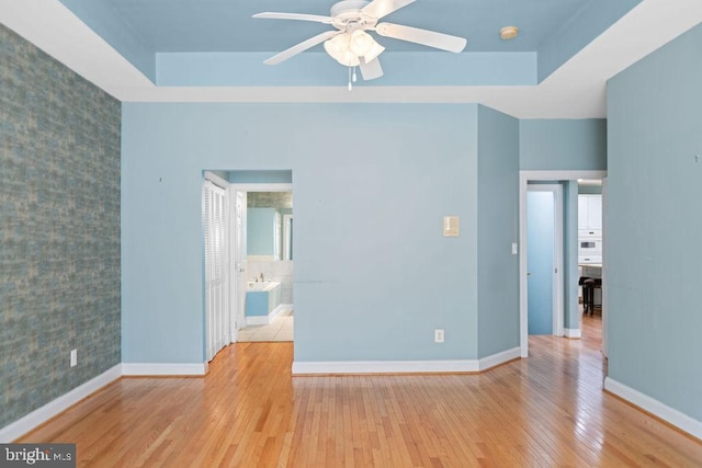 unfurnished bedroom featuring an accent wall, a tray ceiling, hardwood / wood-style flooring, and baseboards