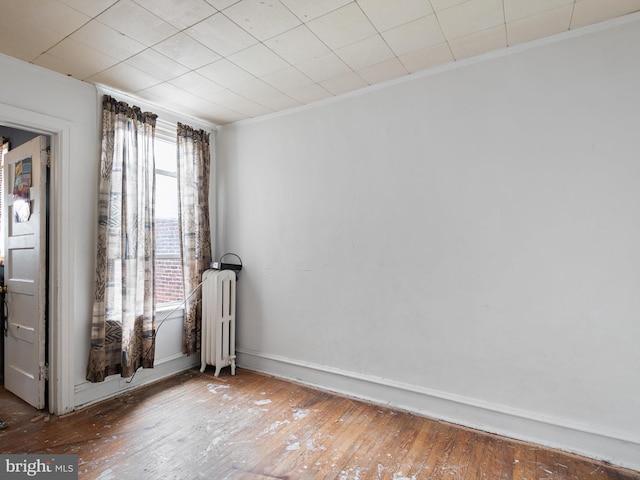 empty room featuring wood-type flooring, radiator heating unit, and ornamental molding