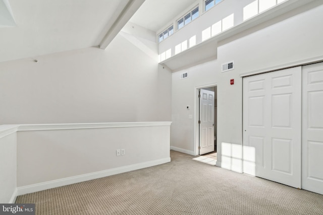 interior space featuring beamed ceiling, a towering ceiling, light colored carpet, and a closet