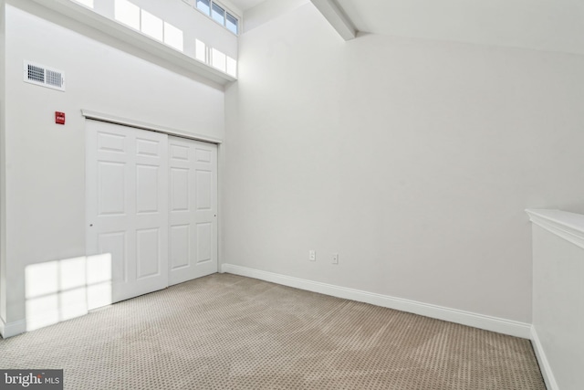 interior space featuring a high ceiling, a closet, light colored carpet, and beamed ceiling