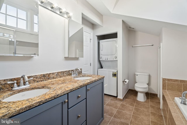 bathroom featuring tiled tub, tile patterned flooring, stacked washer / dryer, vanity, and toilet