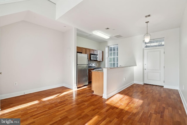 kitchen with hardwood / wood-style flooring, appliances with stainless steel finishes, decorative light fixtures, and kitchen peninsula