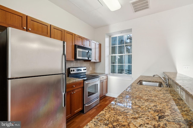 kitchen featuring dark wood-type flooring, sink, dark stone countertops, appliances with stainless steel finishes, and decorative backsplash