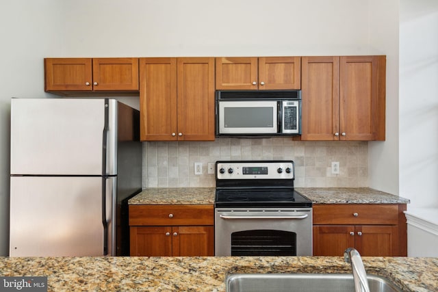 kitchen with tasteful backsplash, appliances with stainless steel finishes, sink, and light stone counters