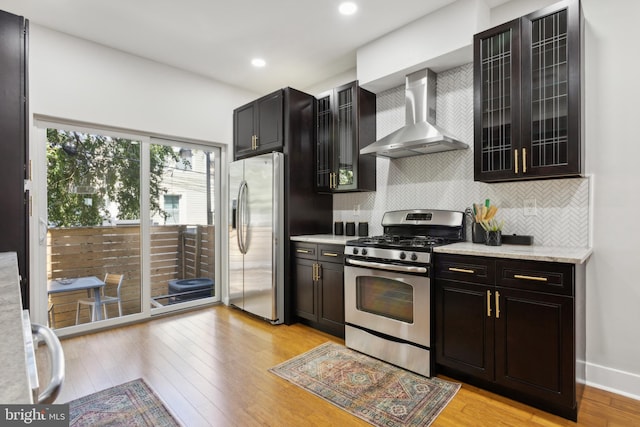 kitchen with appliances with stainless steel finishes, backsplash, wall chimney exhaust hood, and light hardwood / wood-style floors