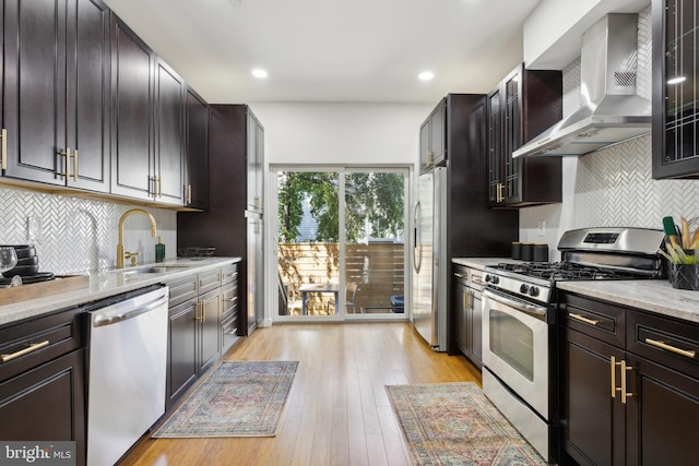 kitchen featuring light hardwood / wood-style flooring, stainless steel appliances, wall chimney range hood, and tasteful backsplash