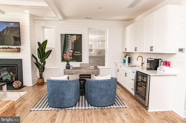 kitchen with beamed ceiling, wooden walls, beverage cooler, white cabinets, and light hardwood / wood-style floors