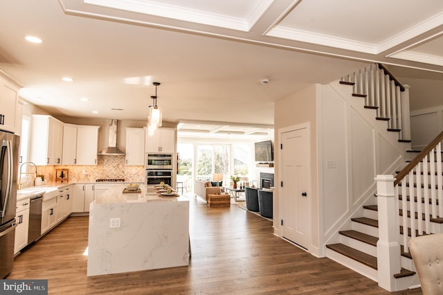 kitchen with a kitchen island, light stone countertops, wood-type flooring, white cabinetry, and wall chimney range hood