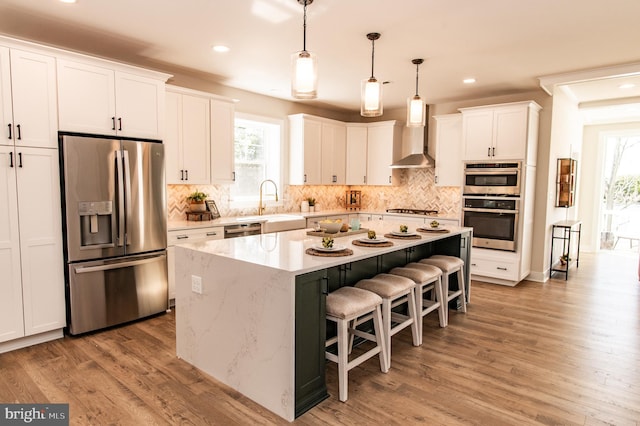 kitchen with a center island, stainless steel appliances, wall chimney range hood, light wood-type flooring, and white cabinets