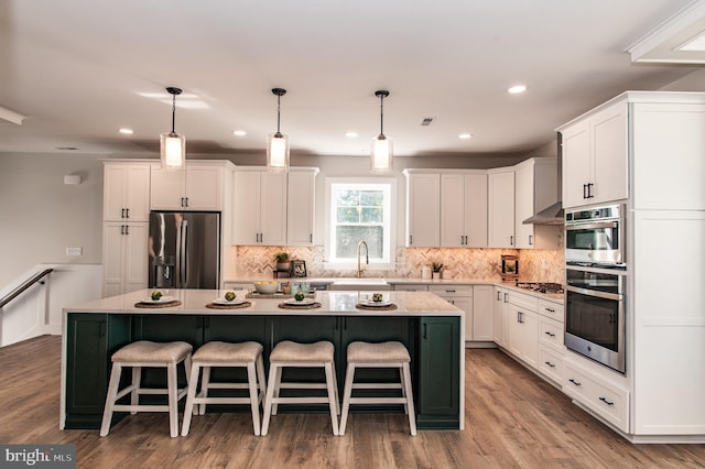 kitchen featuring hardwood / wood-style flooring, stainless steel appliances, white cabinetry, pendant lighting, and a kitchen island