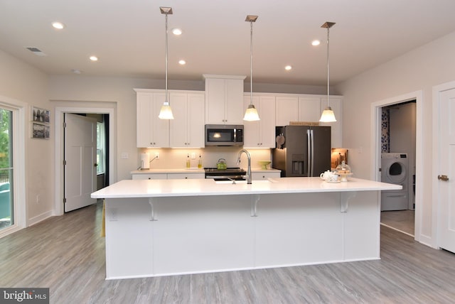 kitchen featuring a large island, light hardwood / wood-style flooring, decorative light fixtures, stainless steel appliances, and washer / clothes dryer