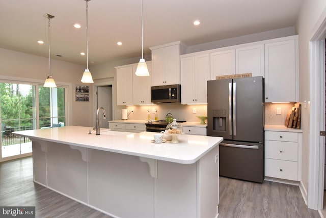 kitchen featuring white cabinetry, decorative light fixtures, an island with sink, appliances with stainless steel finishes, and light hardwood / wood-style floors