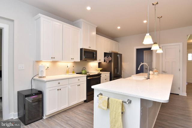 kitchen featuring a center island with sink, appliances with stainless steel finishes, hanging light fixtures, sink, and white cabinetry