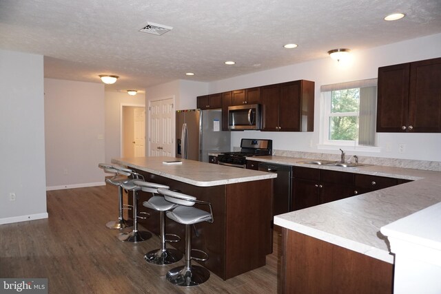 kitchen featuring a textured ceiling, a kitchen island, sink, a breakfast bar, and appliances with stainless steel finishes