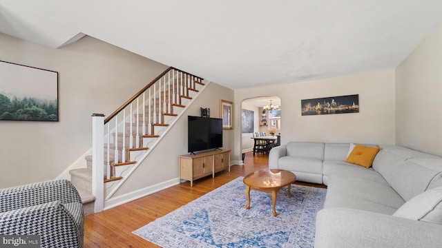 living area featuring wood finished floors, arched walkways, baseboards, a chandelier, and stairs