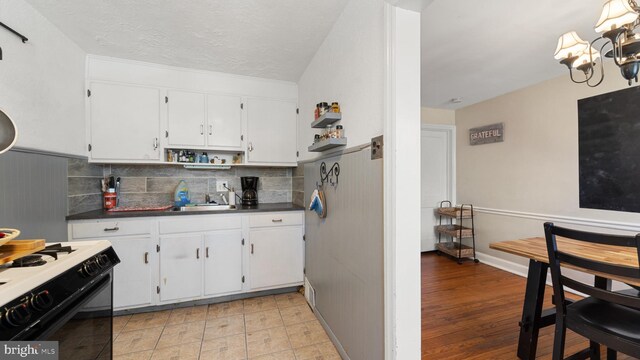 kitchen with white cabinets, backsplash, light hardwood / wood-style floors, a chandelier, and black range oven