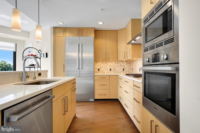 kitchen with light brown cabinetry, exhaust hood, sink, pendant lighting, and built in appliances