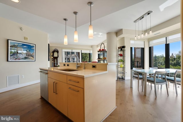 kitchen with sink, dishwasher, light brown cabinets, pendant lighting, and a kitchen island with sink