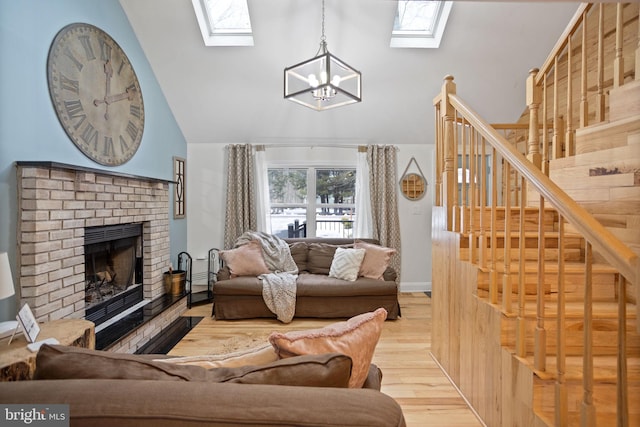 living room with a brick fireplace, a notable chandelier, light wood-type flooring, and vaulted ceiling with skylight