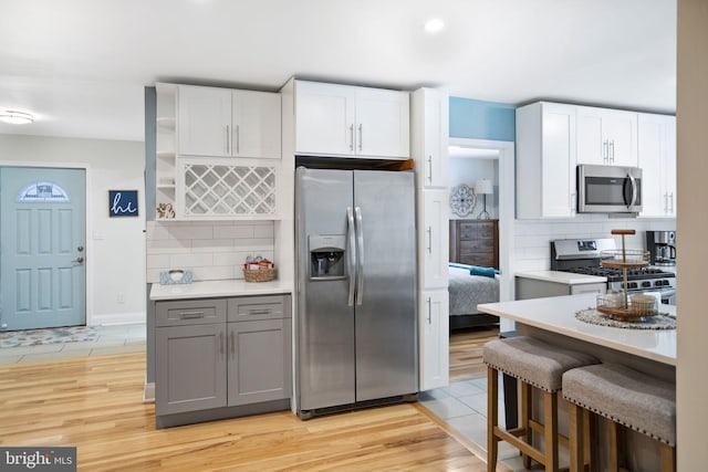 kitchen featuring decorative backsplash, light hardwood / wood-style floors, white cabinets, gray cabinets, and stainless steel appliances