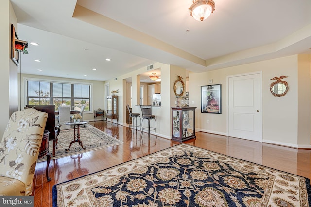 living area featuring a tray ceiling, baseboards, and wood finished floors