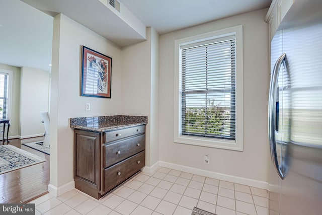 interior space with visible vents, baseboards, dark stone countertops, light tile patterned flooring, and stainless steel refrigerator